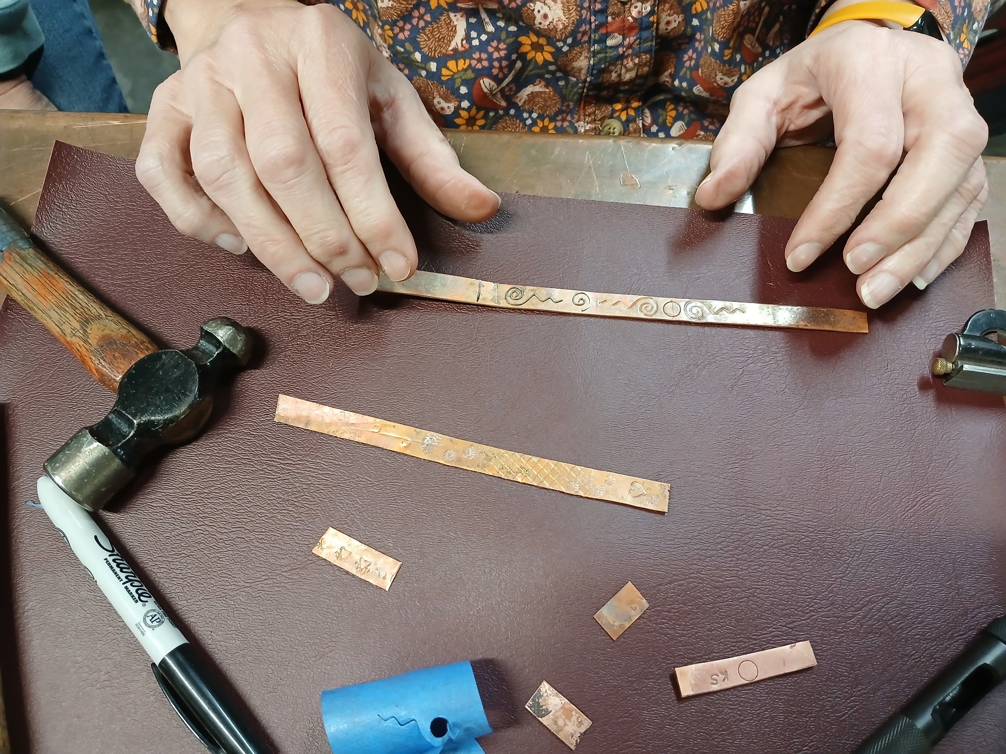 Person working with copper strips and tools on a wooden surface