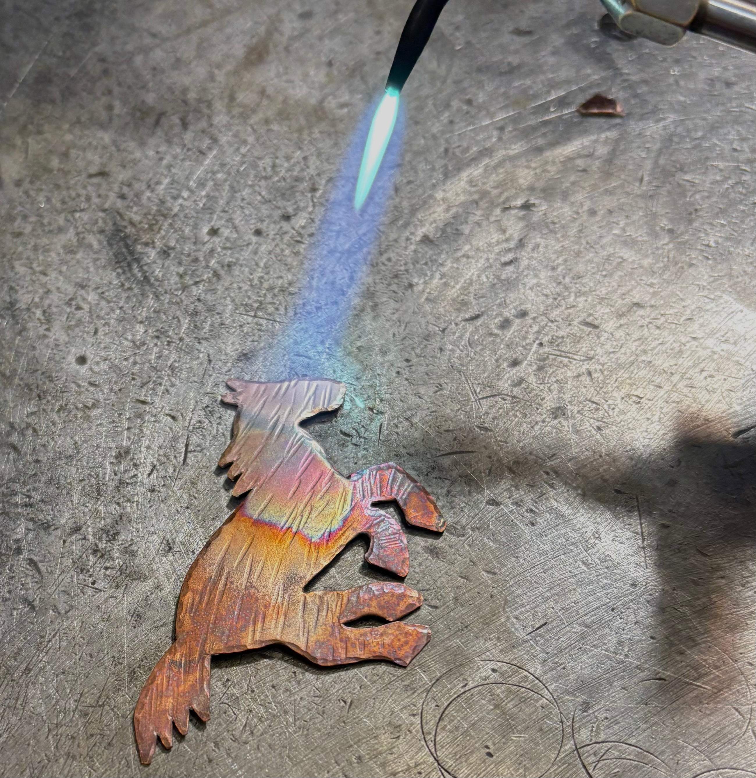 Metal sculpture being worked on with a torch, showing a rainbow effect.