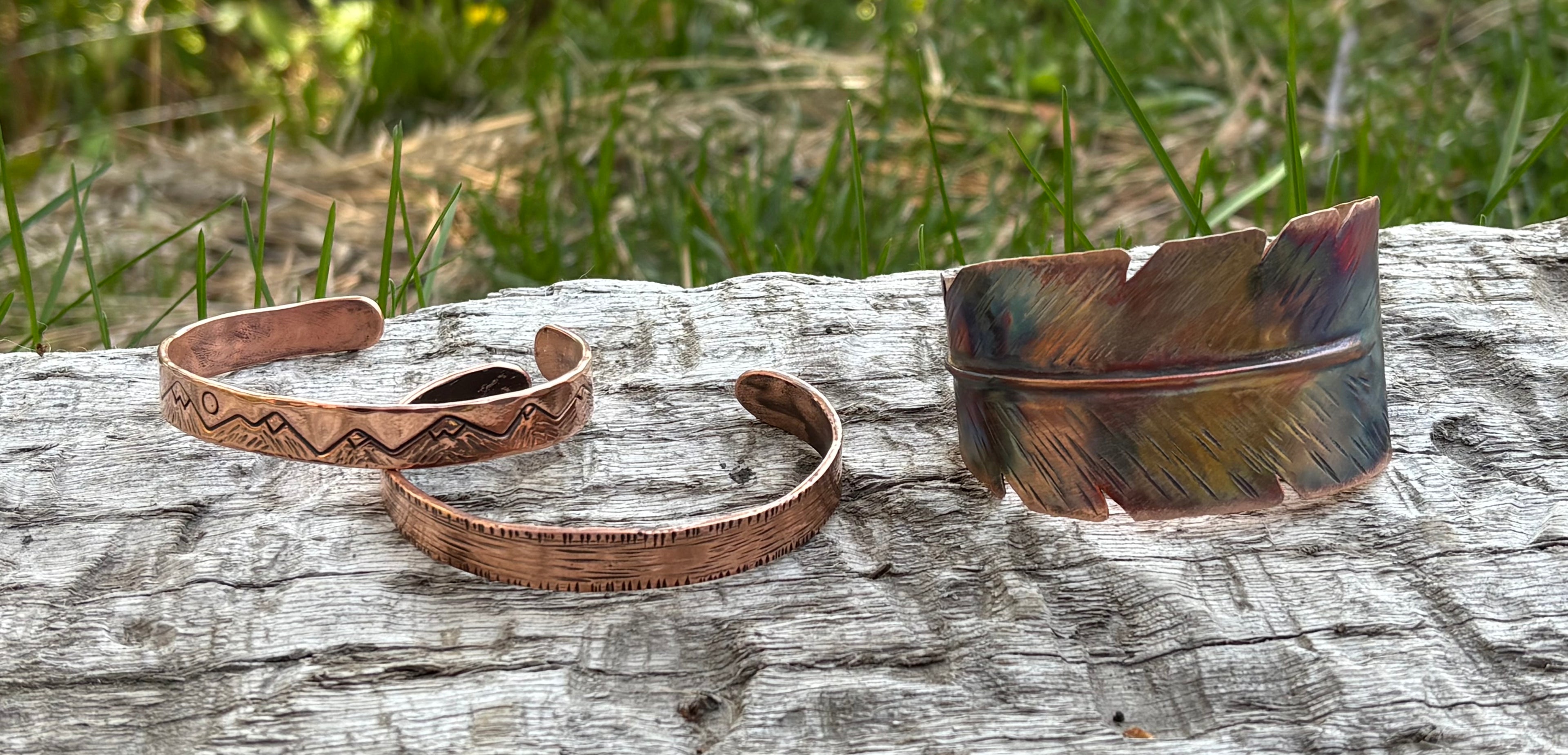 Two copper bracelets on a wooden surface with grass in the background