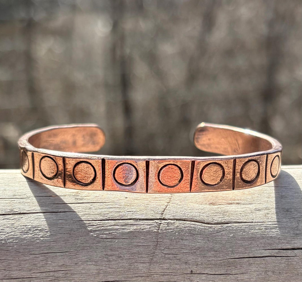 Copper bracelet with engraved design on a wooden surface