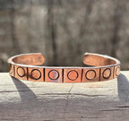 Copper bracelet with engraved design on a wooden surface