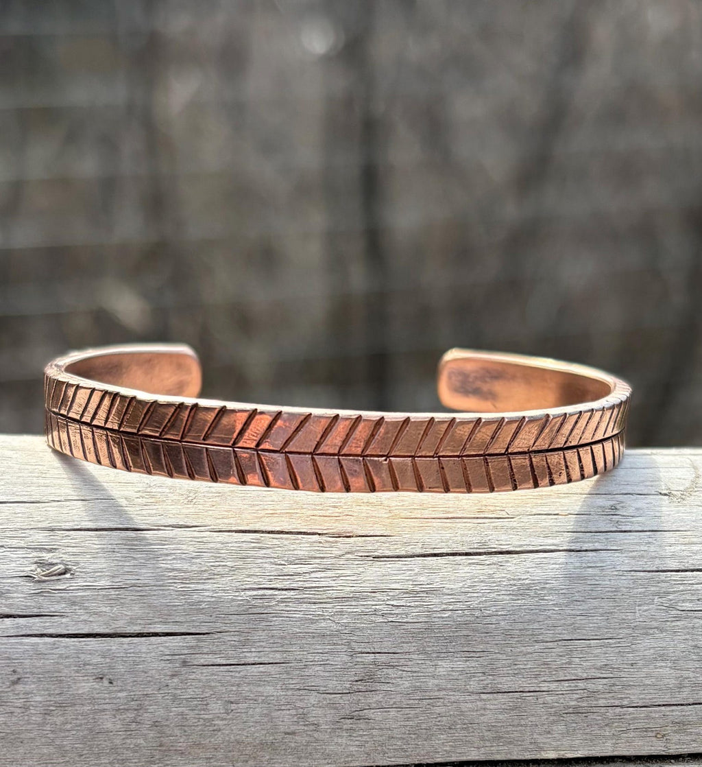 Copper bracelet with textured pattern on a wooden surface