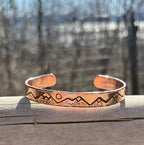 Copper bracelet with mountain design on a wooden surface