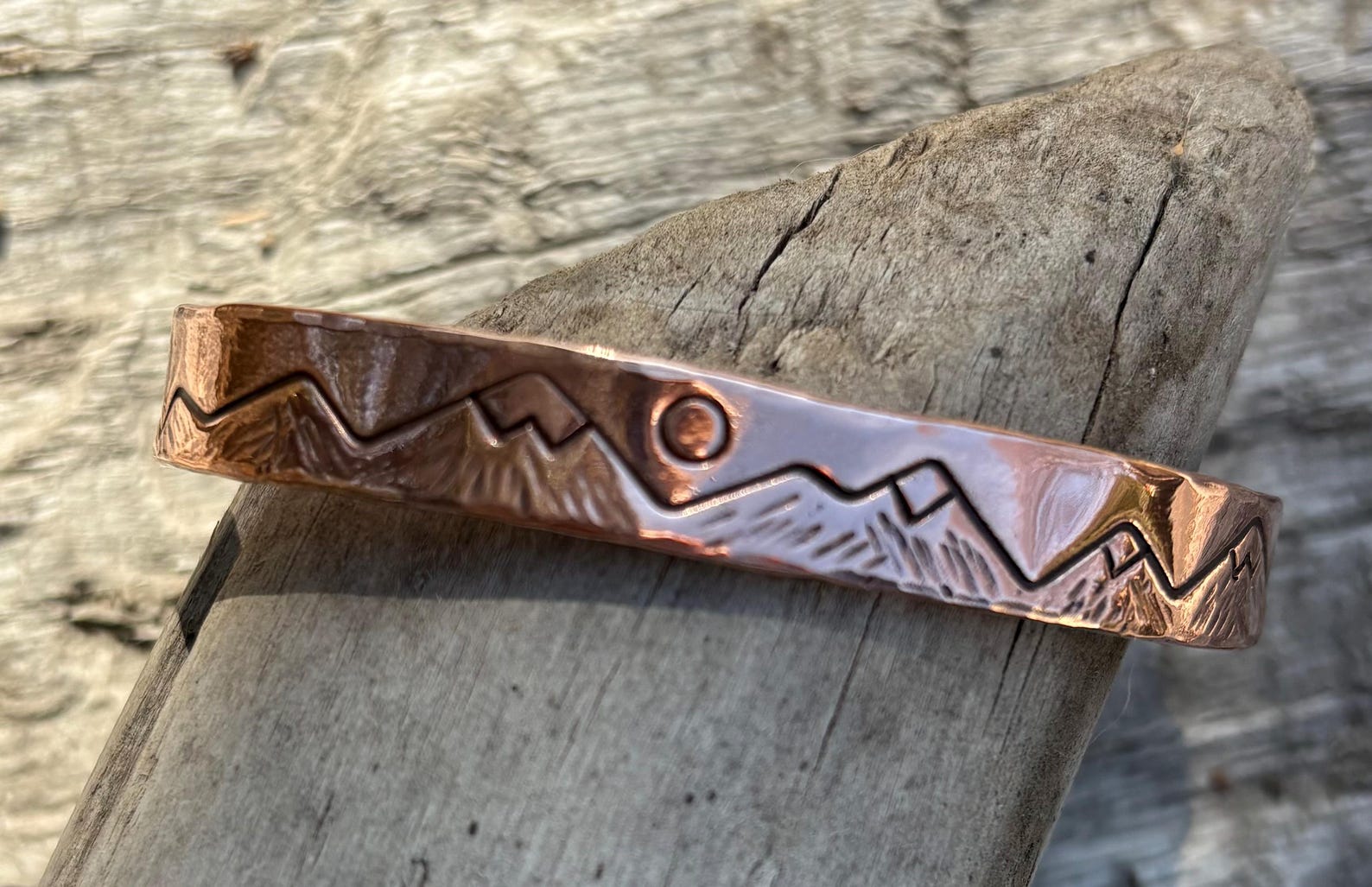 Copper bracelet with mountain design on a wooden surface