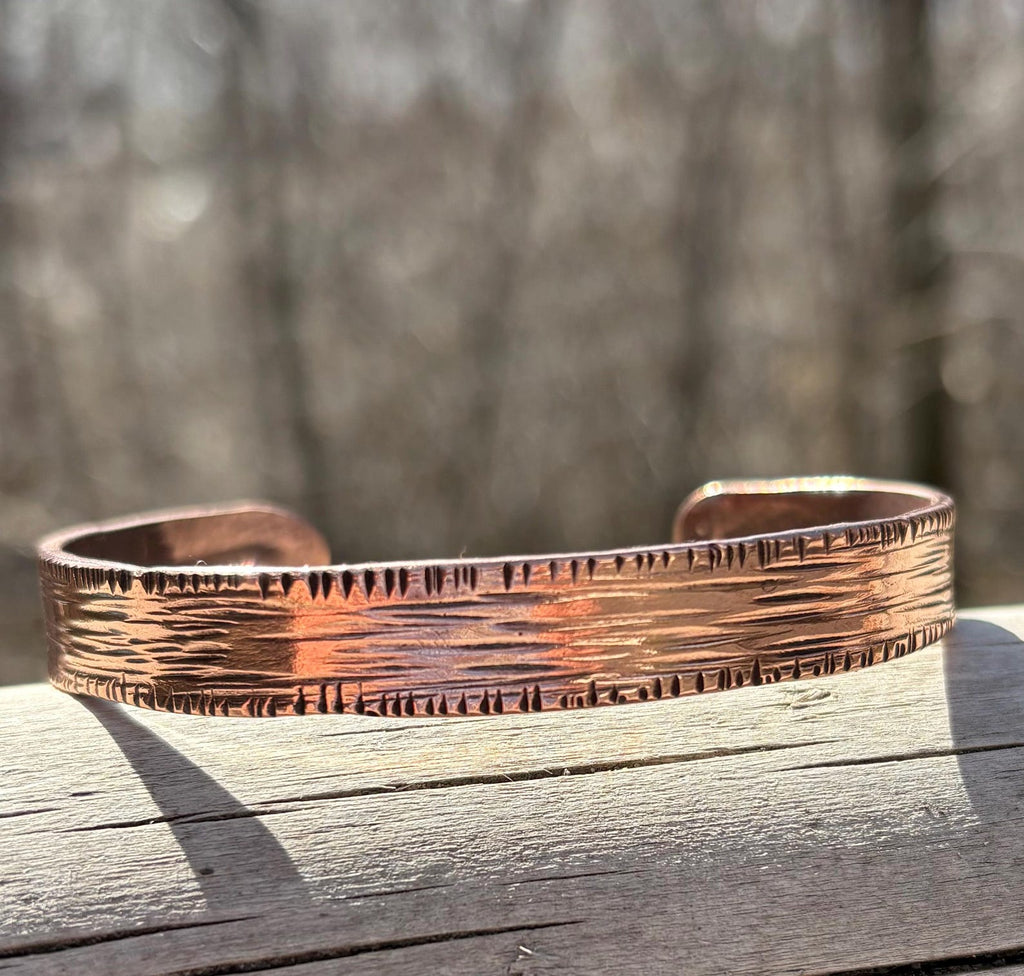 Copper bracelet with textured surface on a wooden surface