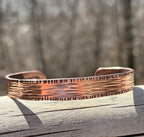 Copper bracelet with textured surface on a wooden surface