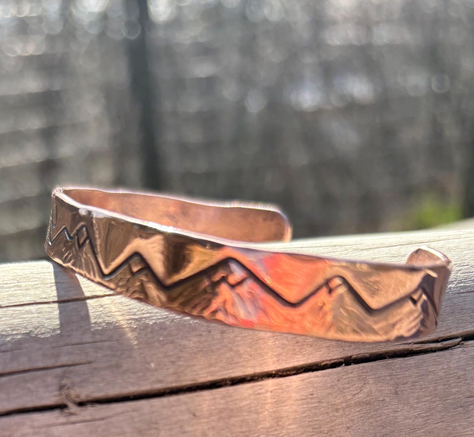 Copper bracelet with mountain design on a wooden surface