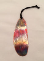 Colorful feather-shaped object with a black string on a beige background