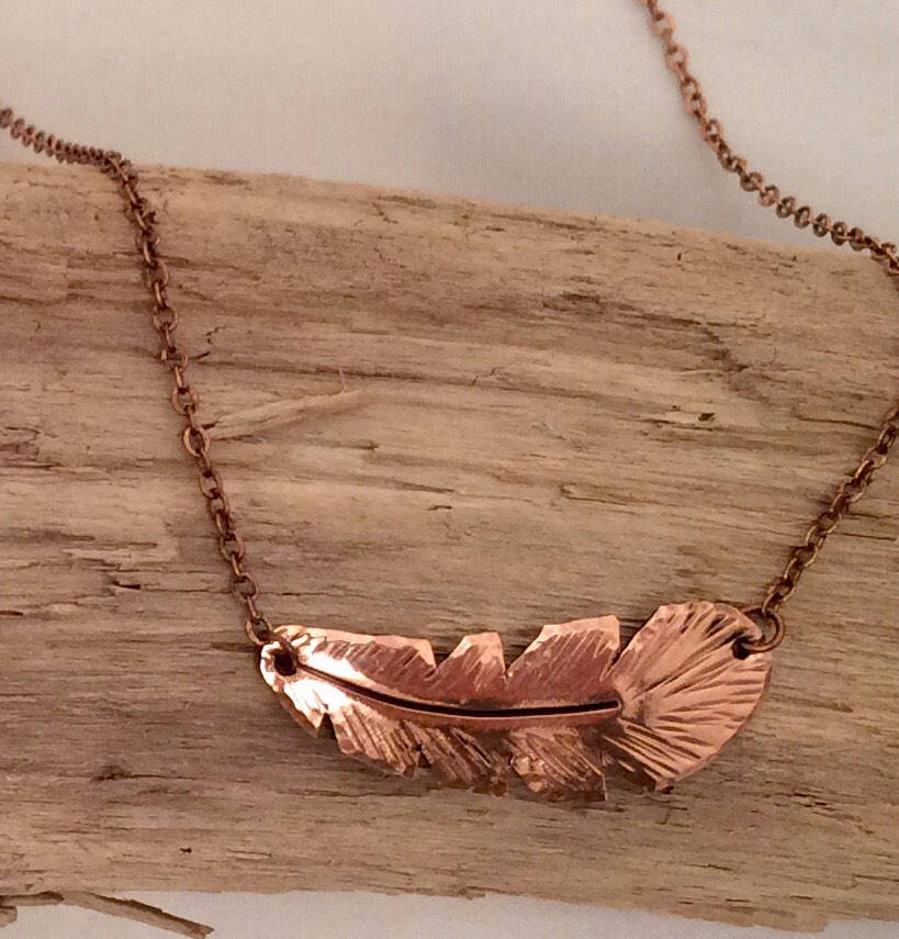 Copper necklace with leaf design on a wooden surface