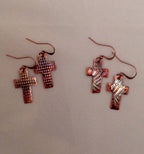Pair of copper cross-shaped earrings on a beige background