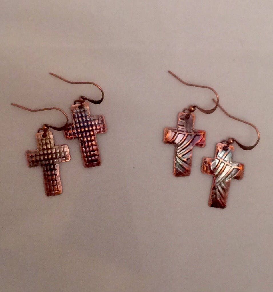 Pair of copper cross-shaped earrings on a beige background