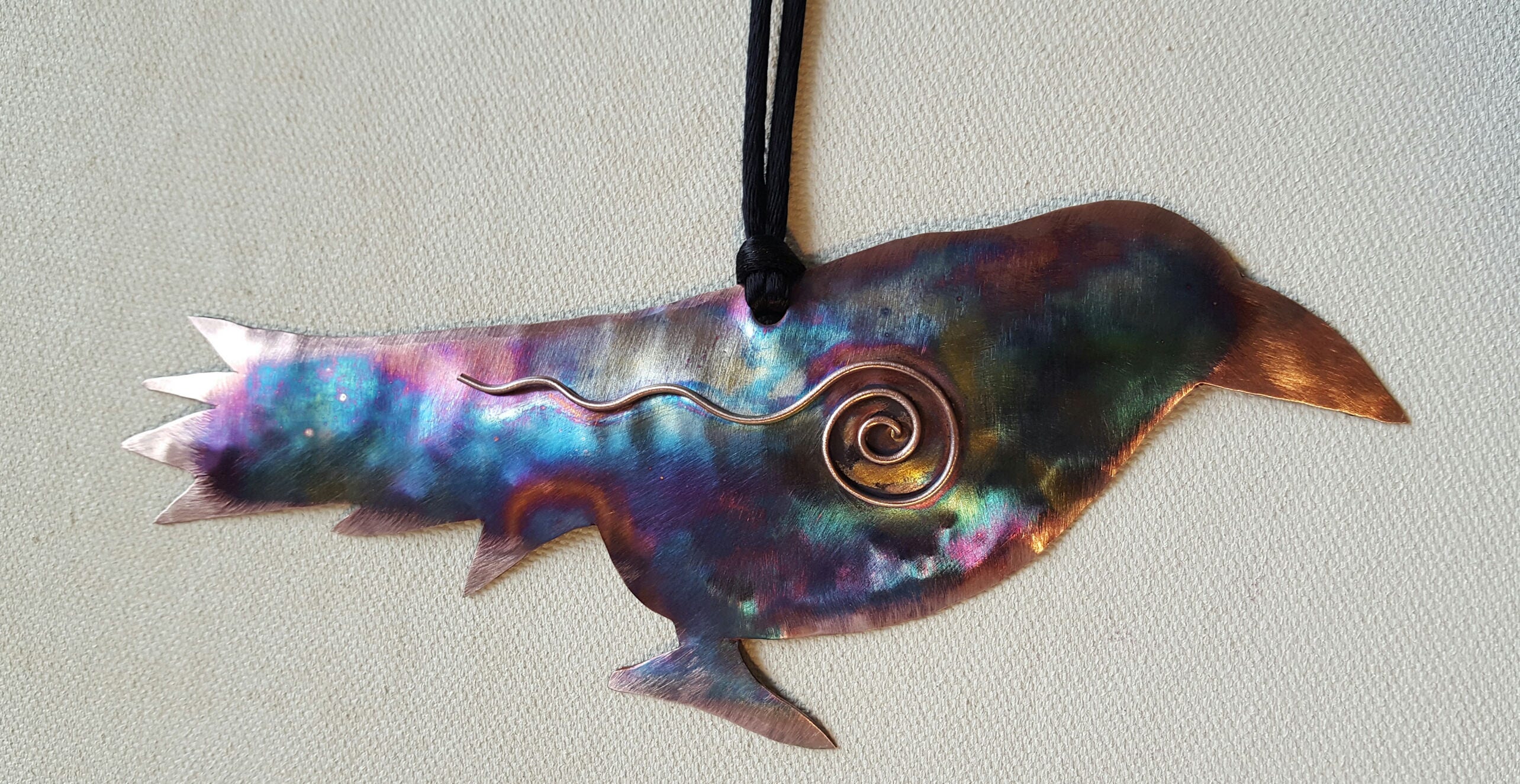 Decorative metal fish ornament with a spiral design on a light gray background