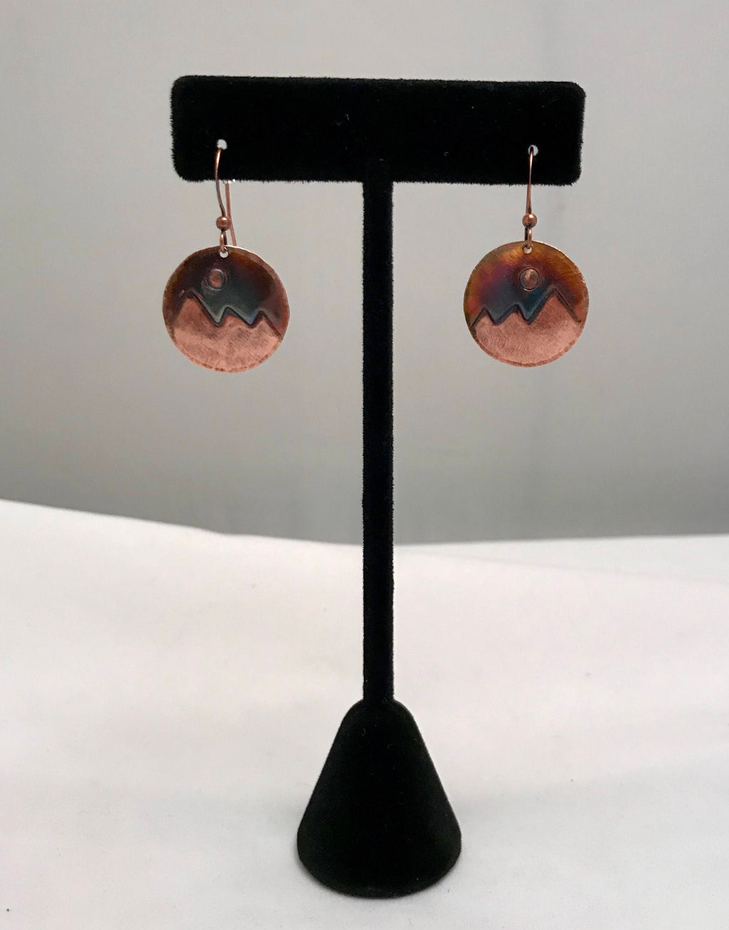Copper earrings on a black earring stand against a gray background