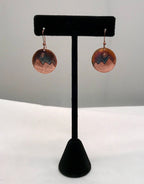 Copper earrings on a black earring stand against a gray background