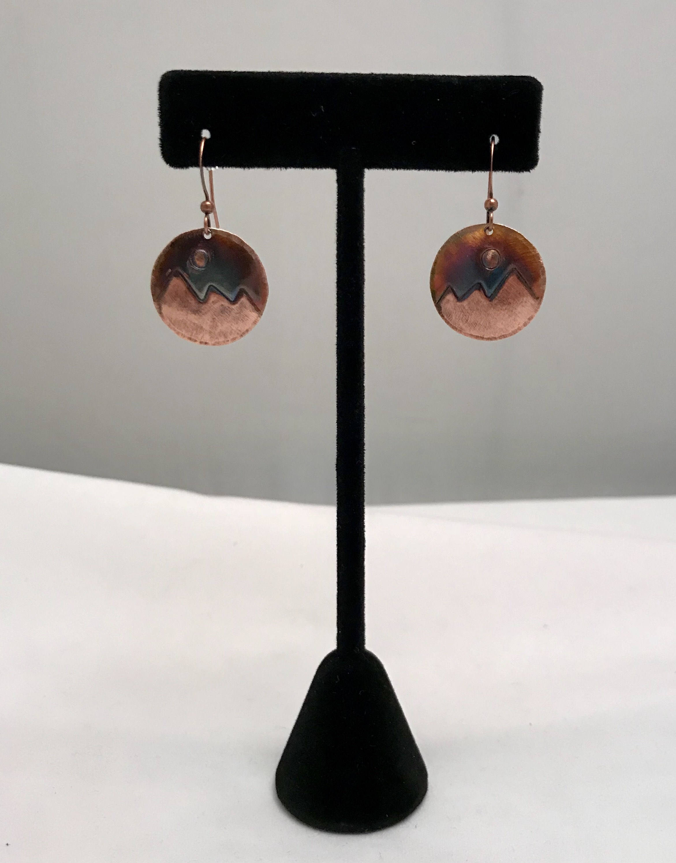 Copper earrings on a black earring stand against a gray background