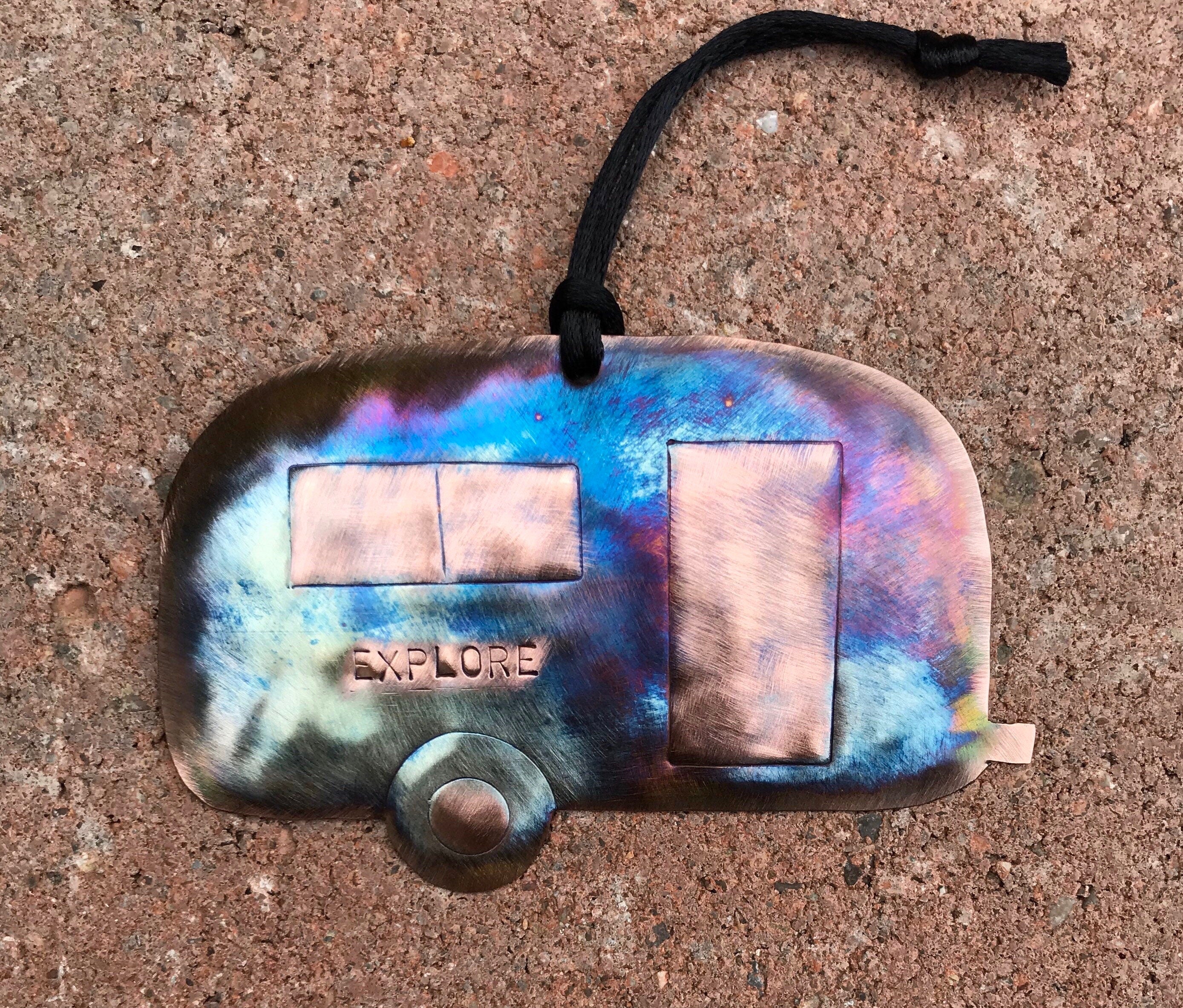 Colorful copper camper ornament with 'EXPLORE' text on a textured surface