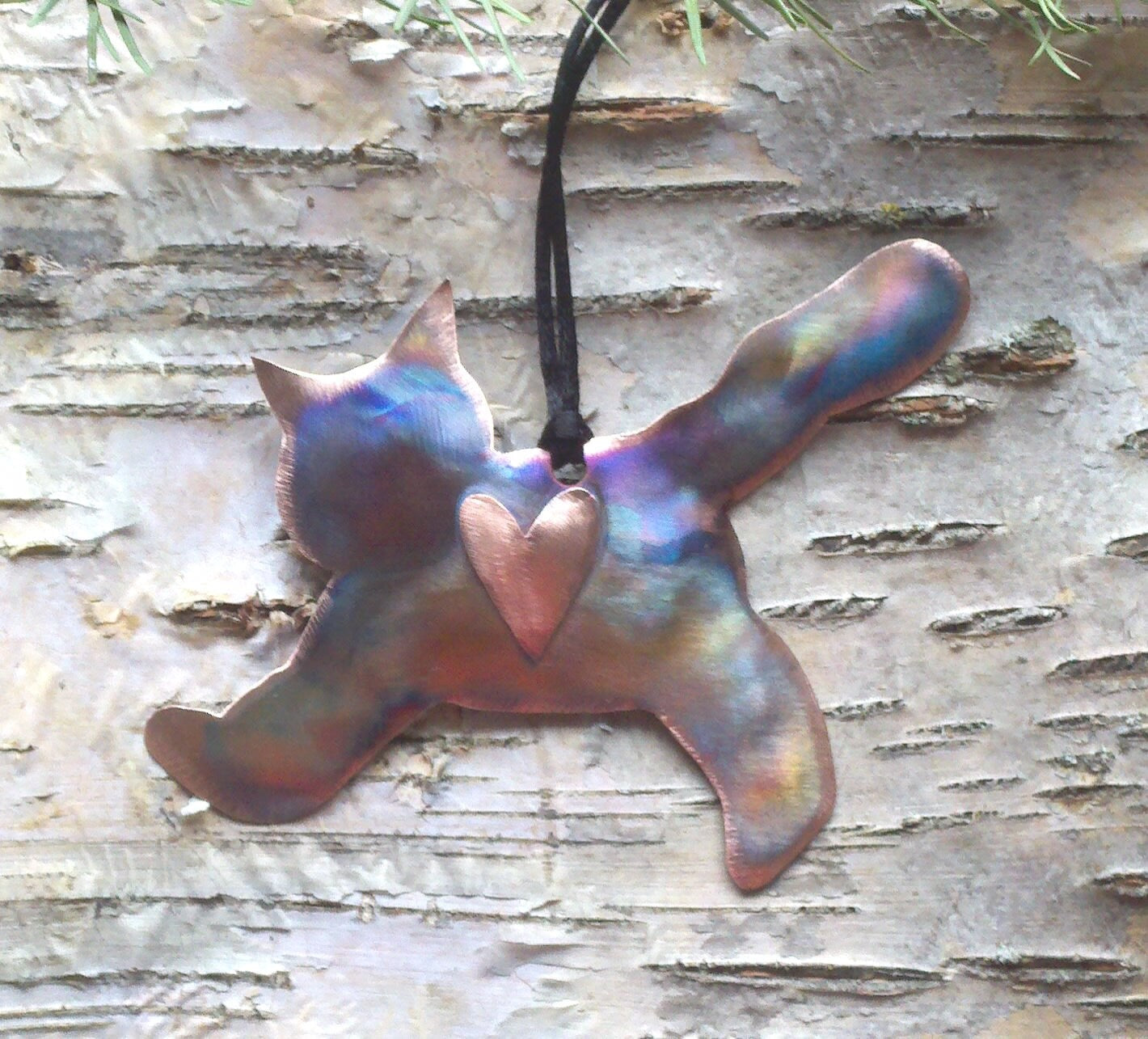 Metallic pendant shaped like a cat with a heart on a wooden surface