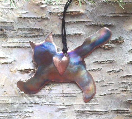 Metallic pendant shaped like a cat with a heart on a wooden surface
