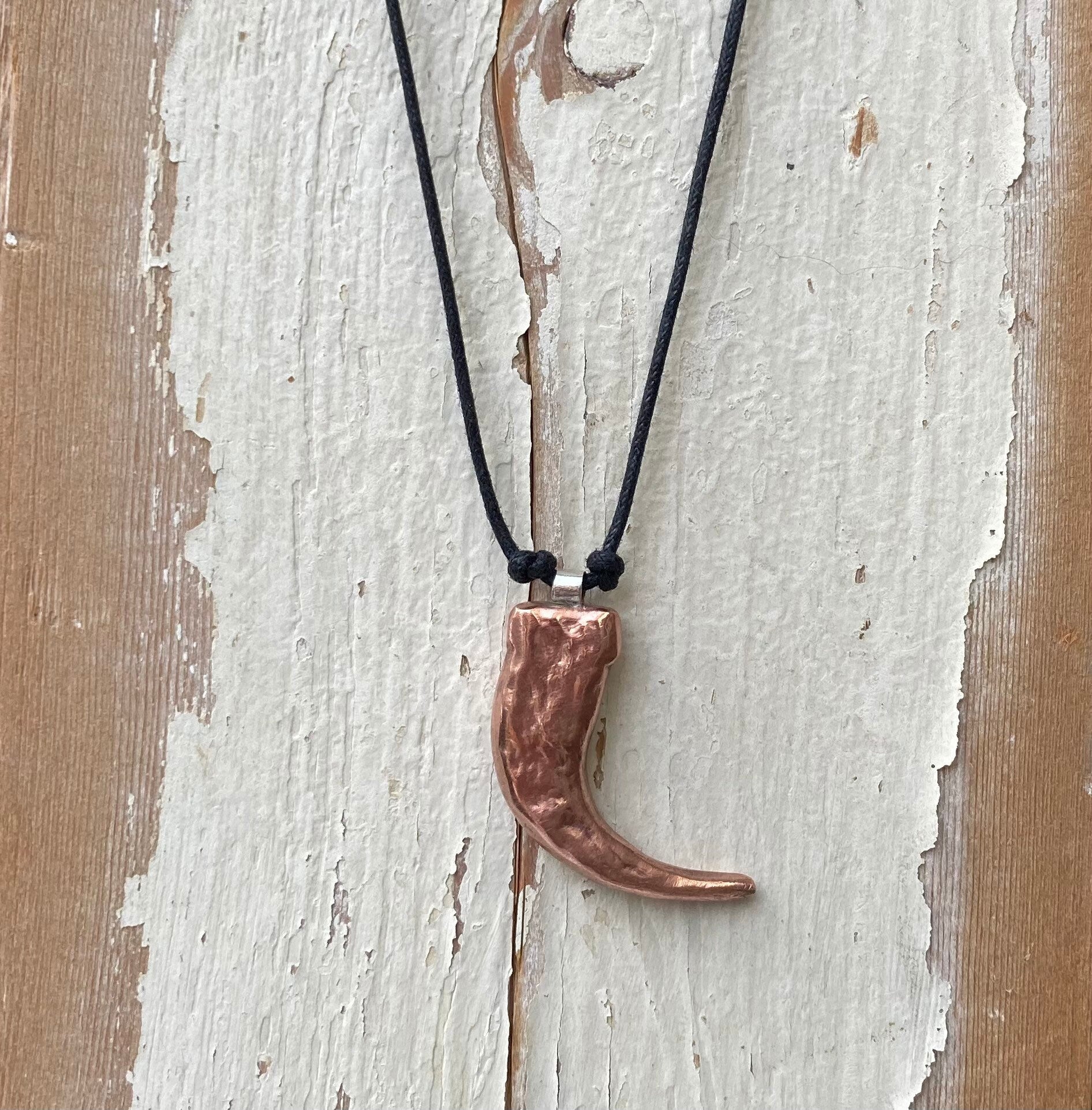 Copper pendant necklace on a black cord against a wooden background