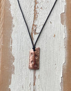 Copper pendant necklace on a black cord against a rustic wooden background