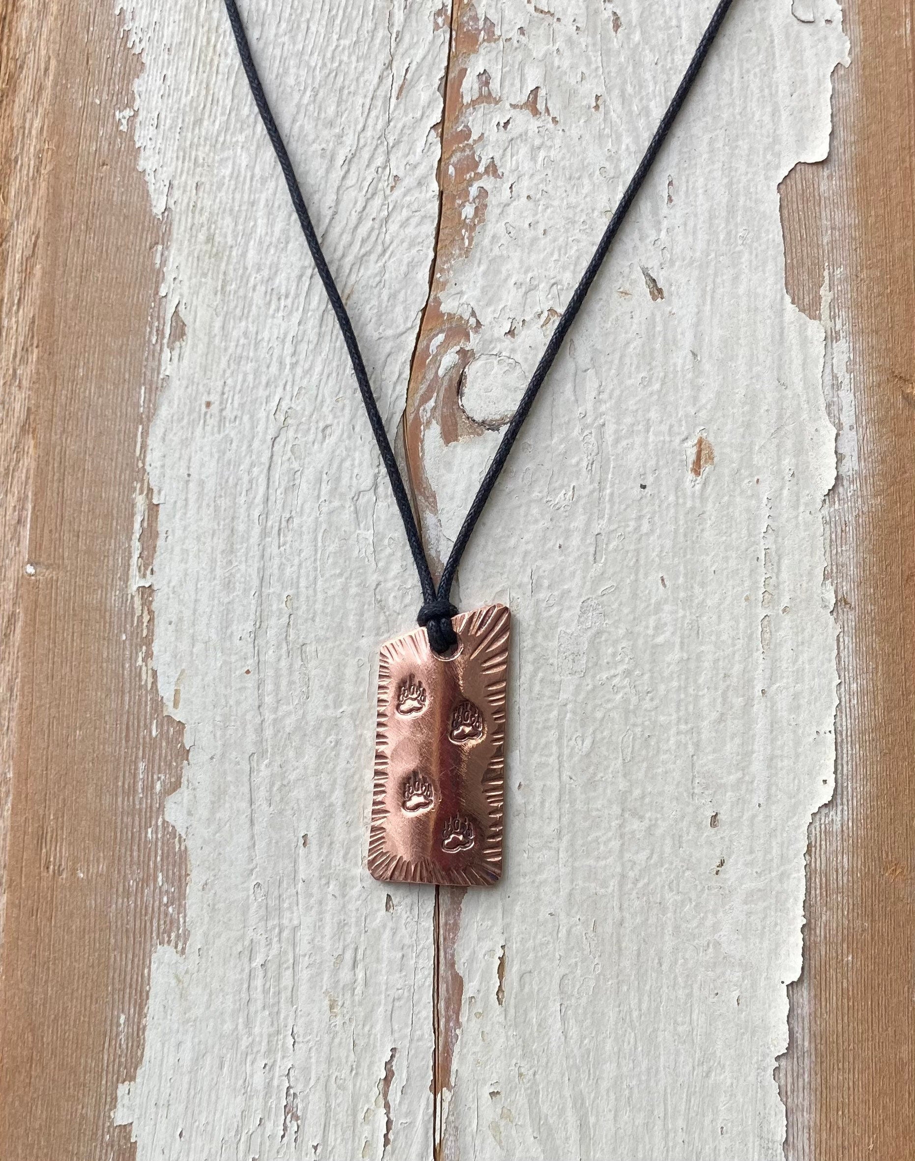 Copper pendant necklace on a black cord against a rustic wooden background